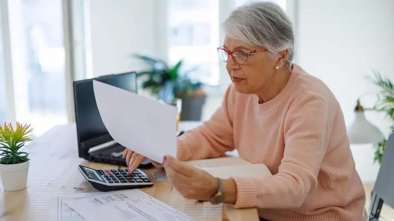 pensive aged woman using laptop paying bills online at home. senior businesswoman work on computer.
